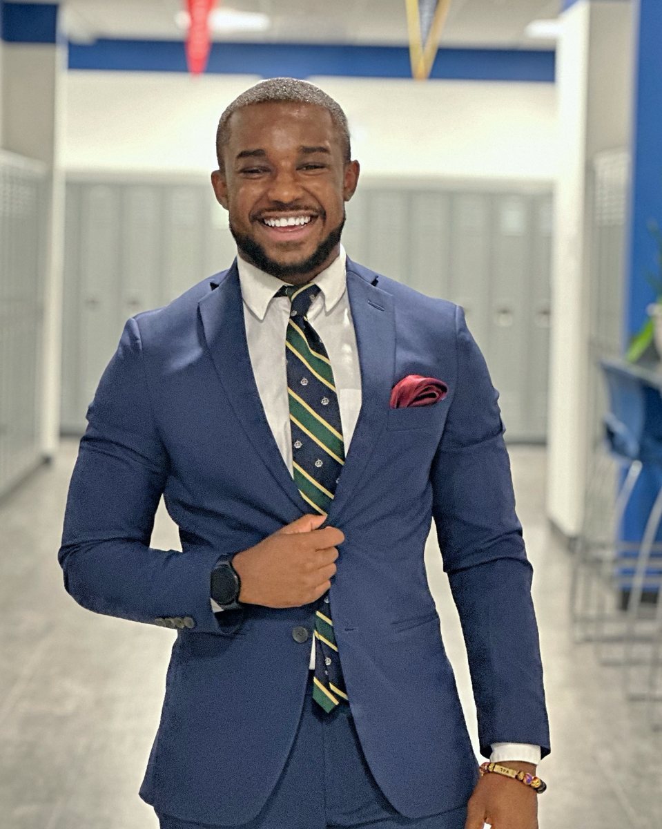 Donald Val, founder of The Persist Foundation, smiling in a navy suit in a school hallway