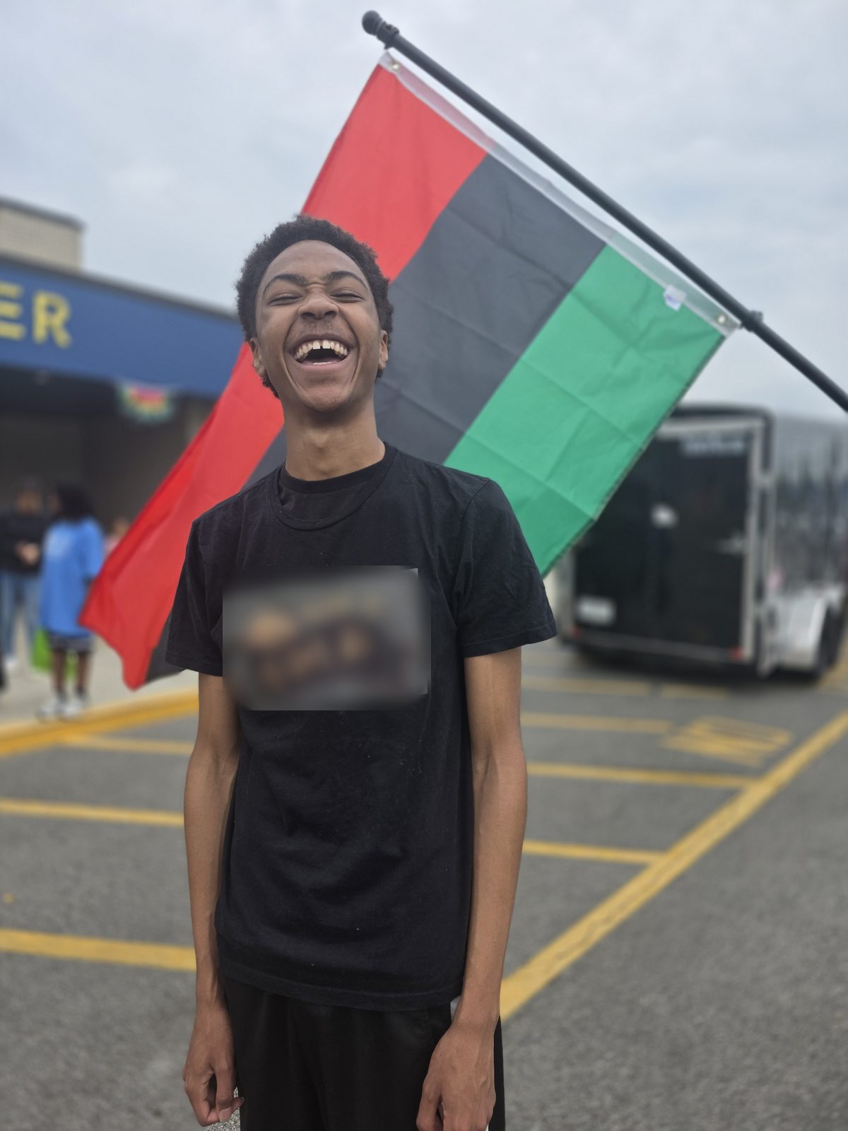 A student in a black T-shirt laughs in front of a red, black and green flag