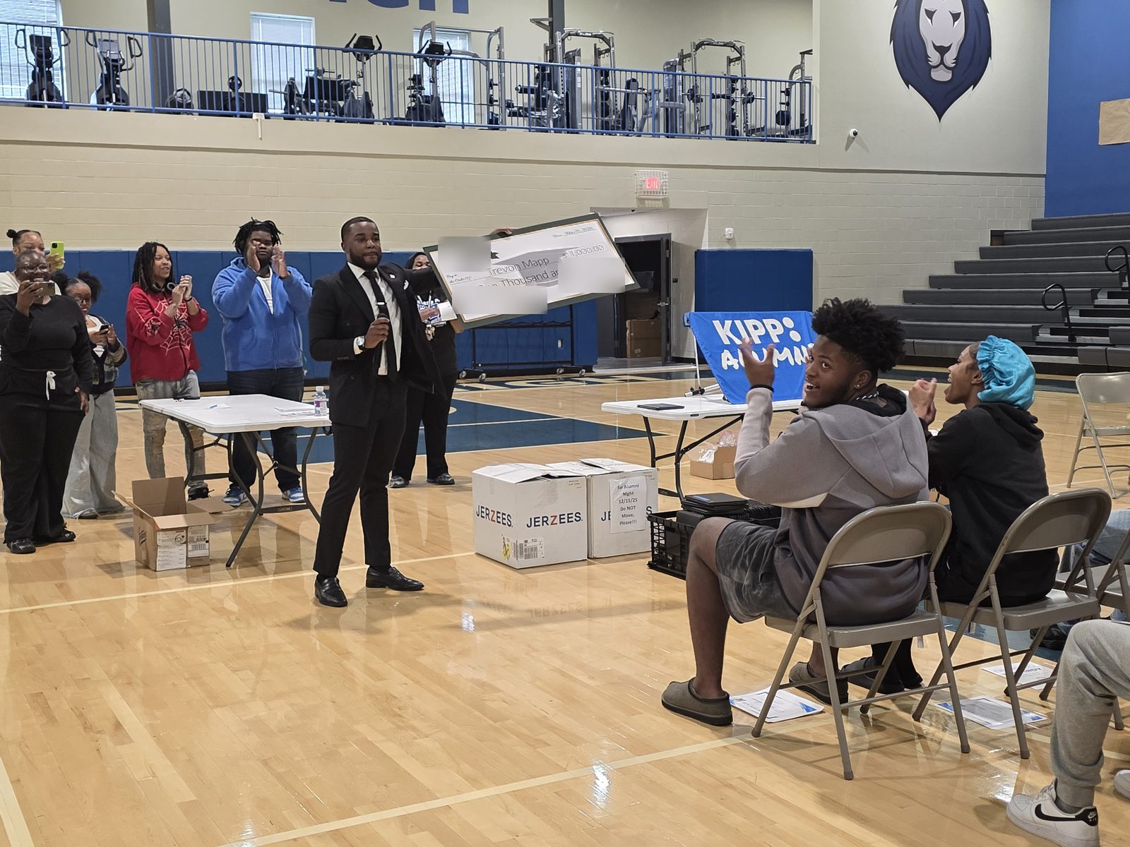 The presenter raises the large check as students and family cheer and take photos