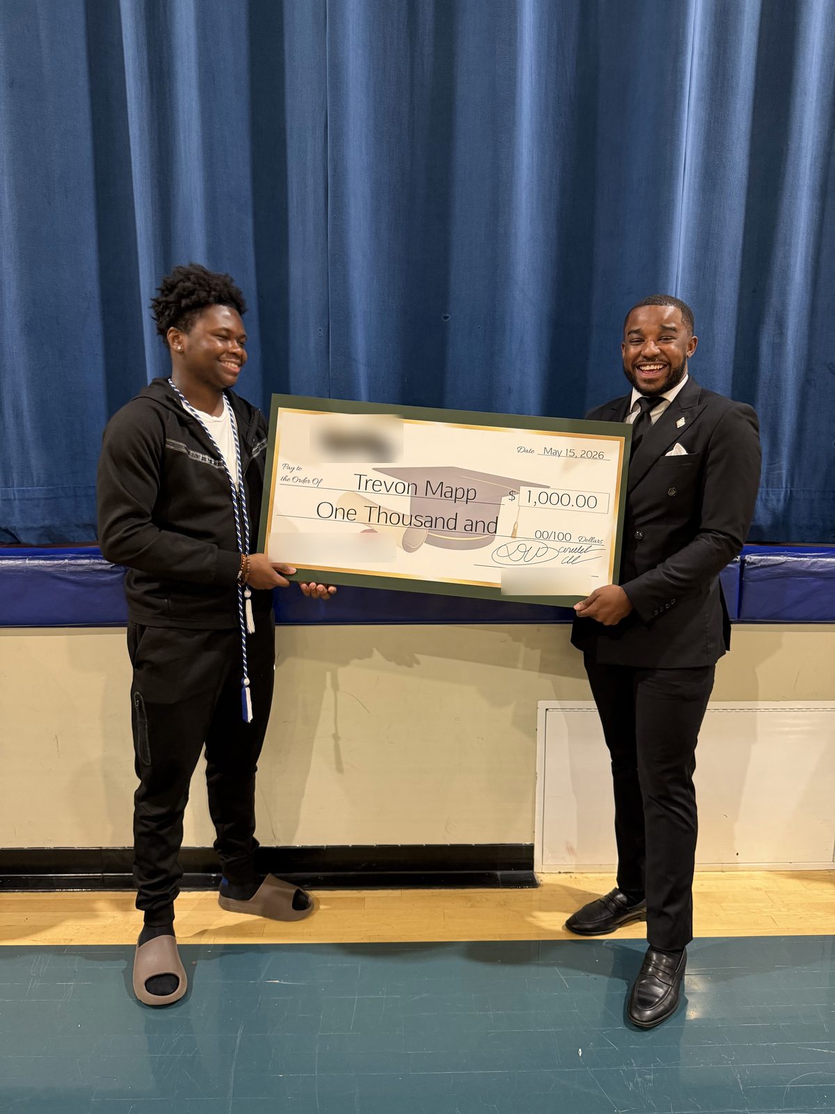 The graduate and presenter hold the scholarship check in front of a blue curtain