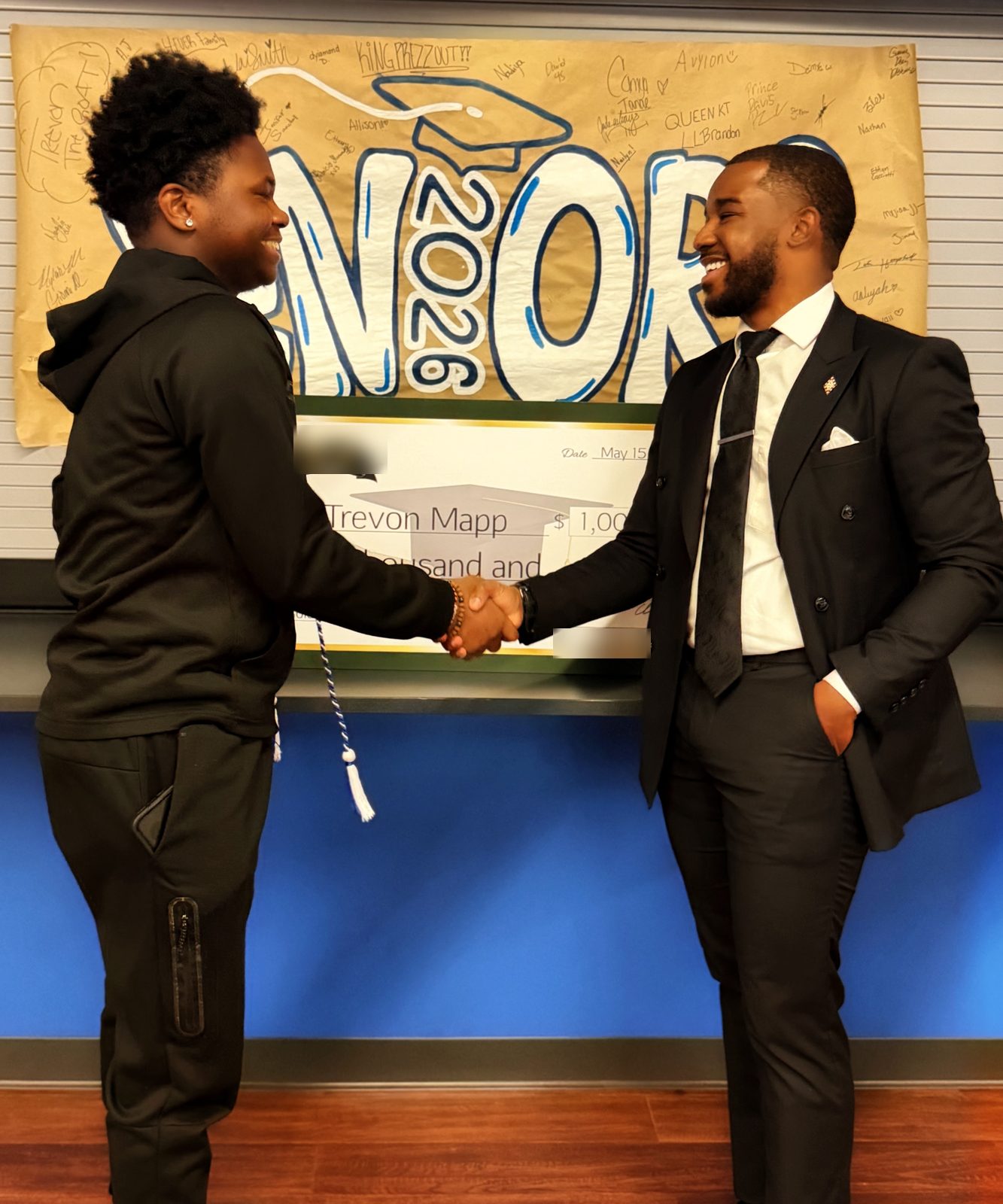 The graduate and presenter shake hands in front of a Class of 2026 seniors banner