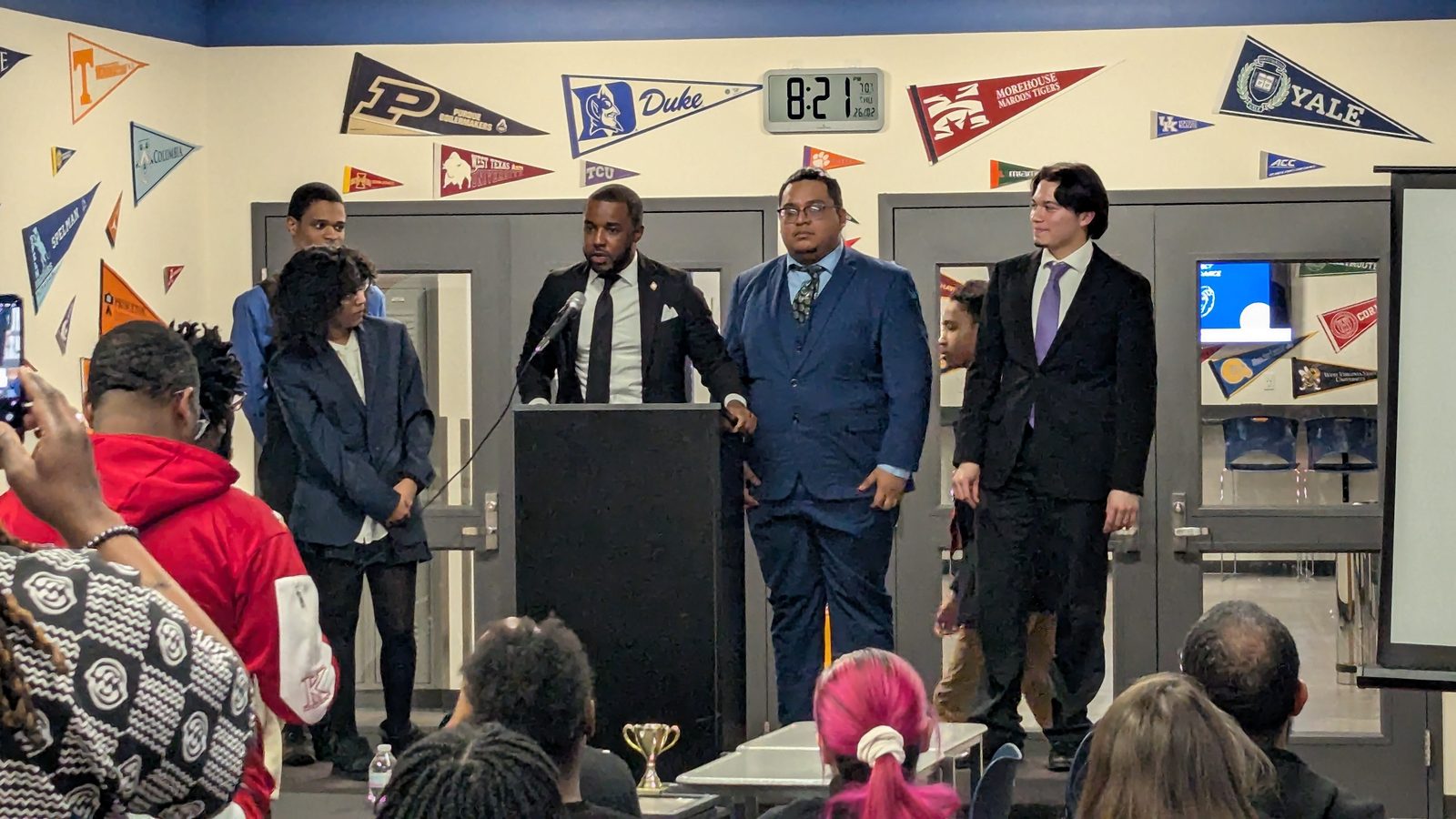 Students and a speaker stand at the front of the room during the debate showcase
