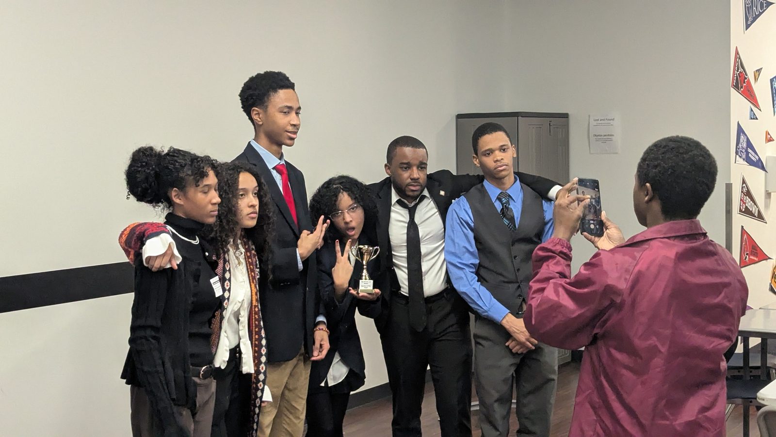 Students in suits pose with a trophy while a classmate takes their photo