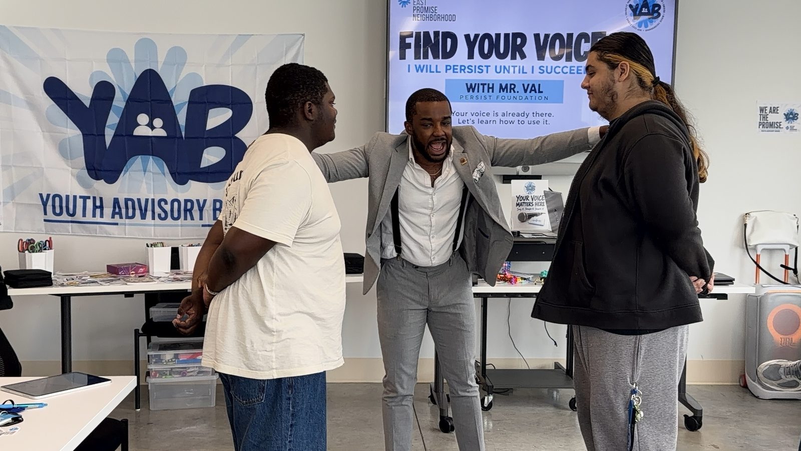 Donald Val coaches two students in front of a screen reading Find Your Voice: I will persist until I succeed, with Mr. Val, Persist Foundation